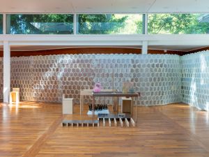 An installation view shows translucent circular panels wrapping through the Korean Pavilion, with sculptural stations placed throughout the sunlit wooden interior.