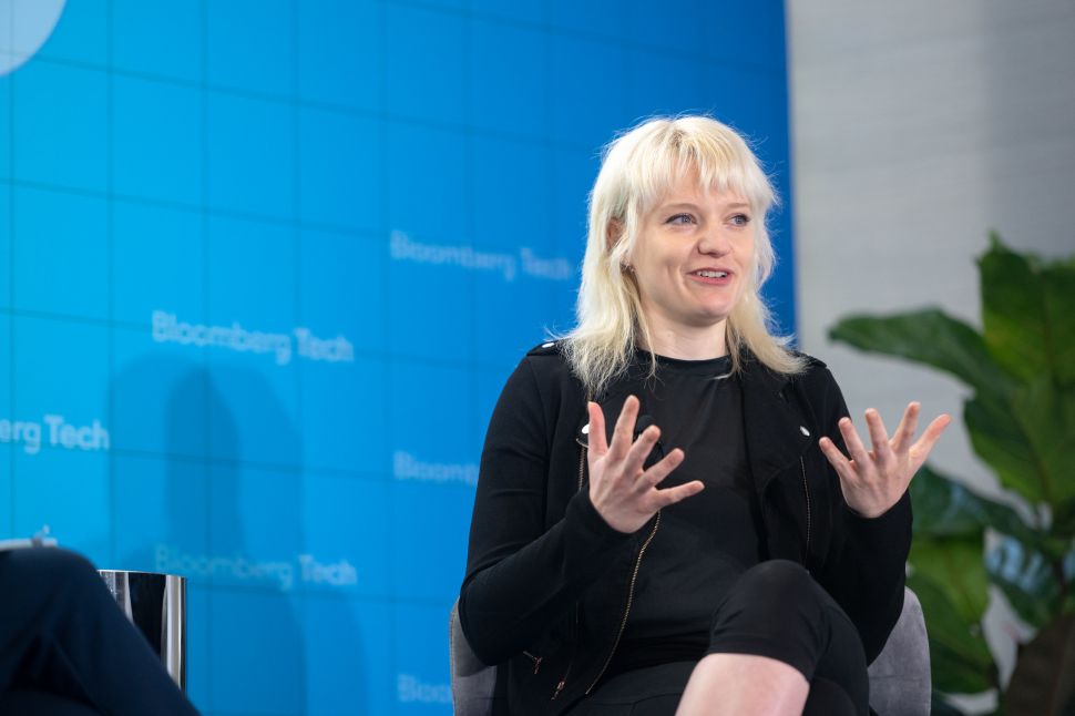 A blonde woman in a black outfit onstage against a blue backdrop