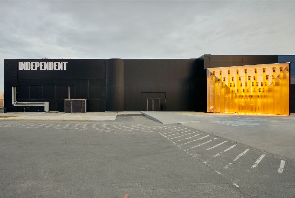 An exterior view of Independent’s black building facade at Pier 36 shows the fair’s entrance glowing in warm yellow light.