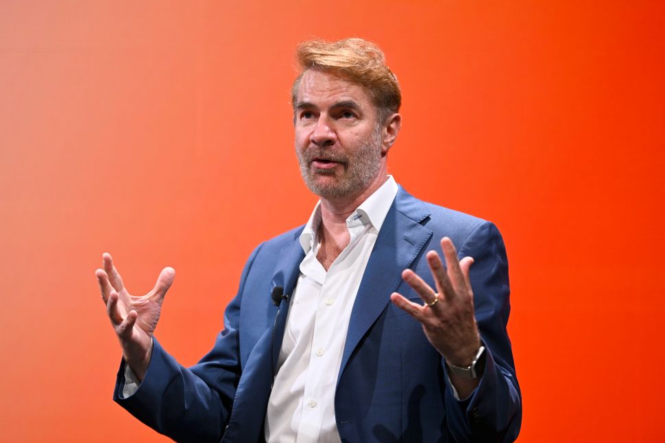 Man in navy suit stands onstage in front of orange background