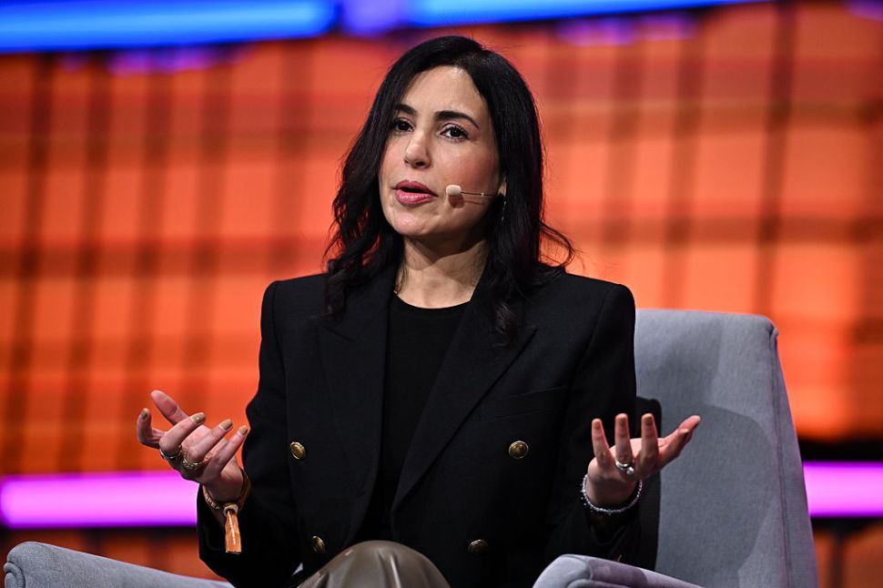 A dark-haired woman in a black outfit speaking onstage.
