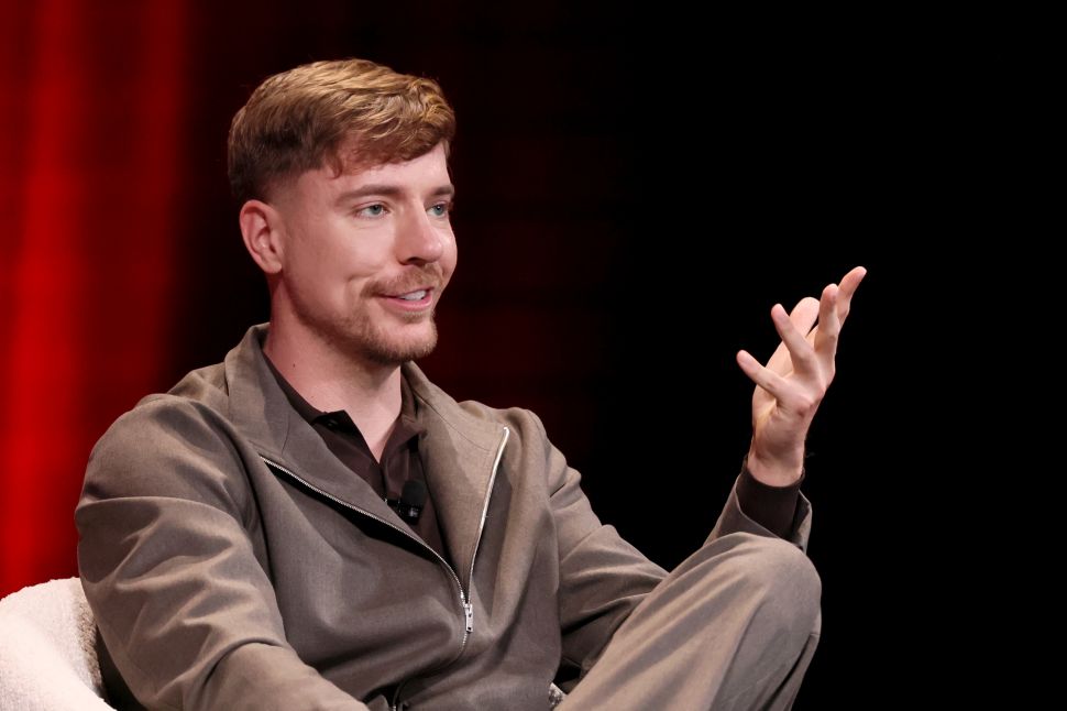 Man in beige suits sits in chair onstage