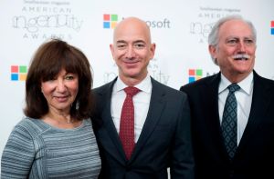 Image of woman in dress and two men in suits posing on red carpet
