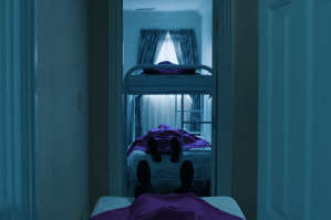 A dimly lit image of bunch beds where people covered in angular purple sheets lay